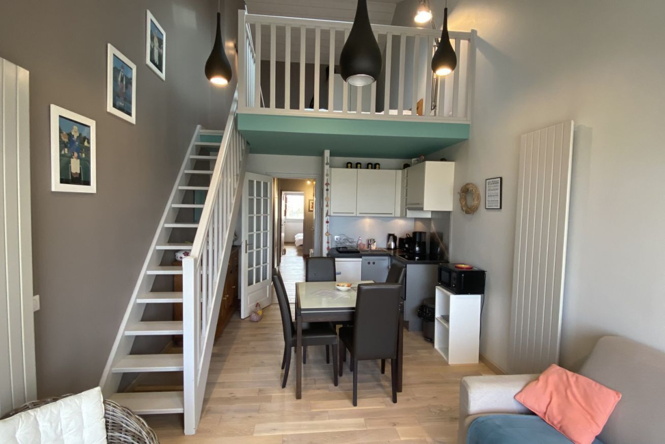 Ett bostadsutrymme i flera nivåer med en trappa, matplats, kök och sittgrupp.