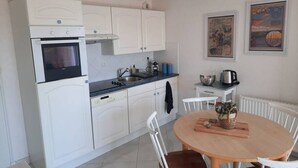 Une cuisine avec des meubles blancs, une cuisinière, un évier et une table à manger avec des chaises.