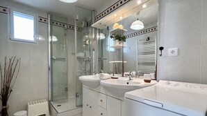 Une salle de bain moderne dotée d’une douche à parois de verre, de deux vasques et d’un lave-linge encastré.