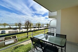 Ein Balkon mit Glastisch und Stühlen, der auf einen Parkplatz und ein Gewässer blickt.