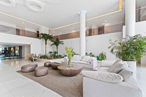 Un vestíbulo amplio con diseño moderno, que cuenta con una zona de estar con sofás y otomanas, una mesa de centro y una planta grande en maceta.
