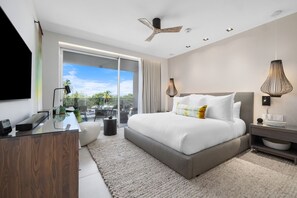 A modern bedroom with a large bed, a desk, a chair, and a view of the outdoors.