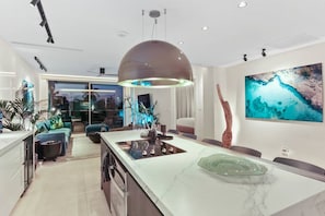 A modern kitchen with a large island, pendant lighting, and a view of the outdoors.