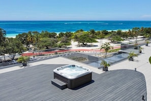 Eine Dachterrasse mit Whirlpool, Blick auf den Ozean und einer angelegten Grünfläche mit Bäumen und einem Weg.