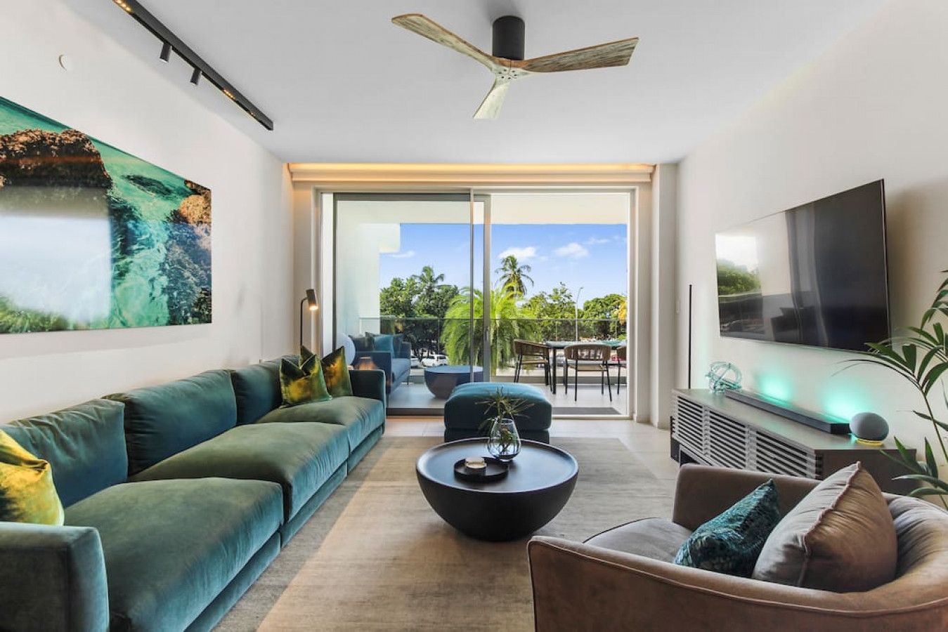 A modern living room with a sofa, coffee table, and TV, featuring a large window and a ceiling fan.
