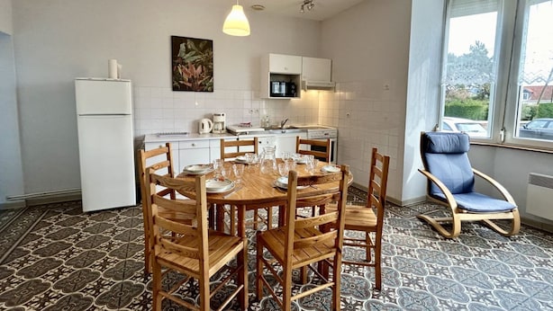 A compact kitchen with a dining table set for six, a refrigerator, a coffee maker, and a window with a view of the outside.