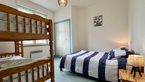 A bedroom with a bunk bed, a single bed, a bedside lamp, and a door with a blue frame.
