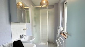 A modern bathroom with a white sink, a black towel, a glass shower enclosure, and a mirror.