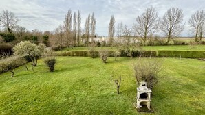 A well-maintained grassy area with a stone structure, possibly a fountain or sculpture, surrounded by trees and hedges. - La pommeraie 4, apartment for 4 people (Quend)