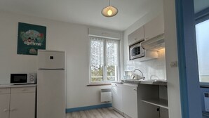 A modern kitchen with white cabinets, a microwave, a refrigerator, a sink, and a window with a view of trees. - La pommeraie 4, apartment for 4 people (Quend)