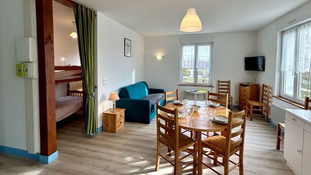 A cozy room with a bunk bed, a blue sofa, a dining table with chairs, and a TV on the wall. - La pommeraie 4, apartment for 4 people (Quend)