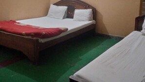 Una cama individual con cabecera de madera y ropa de cama blanca en una habitación con alfombra verde y paredes beige.