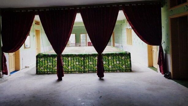 Una habitación vacía con un banco de estampado floral verde, cortinas rojas y vistas a un edificio.