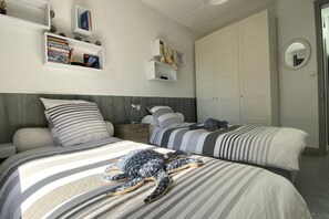 Un dormitorio con dos camas, un armario, una mesita de noche y una estantería con libros y objetos decorativos.