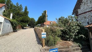 Ein Schotterweg führt zu einem Gebäude mit einer Steinaußenwand, einem Holzzaun und einem Schild, das einen Parkplatz kennzeichnet.