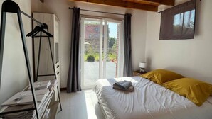 Ein Schlafzimmer mit Bett, Holzboden, einem Fenster mit Vorhängen und Blick nach draußen.