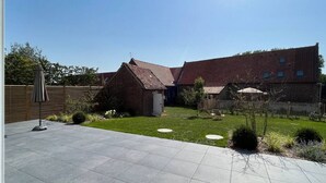 Ein Innenhof mit einem Backsteingebäude, einer gepflasterten Terrasse und einem Holzzaun.