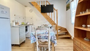 Une cuisine avec une table à manger, des chaises, un escalier en bois, un téléviseur fixé au mur et un meuble contenant de la verrerie.