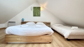 Une chambre avec un grand lit, un plus petit lit, une lampe fixée au mur et une d écoration murale verte.