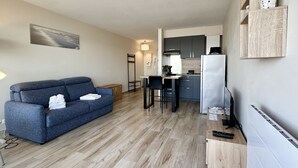 Een moderne woonkamer met een blauwe bank, een kleine keuken met een koelkast, en een eethoek.