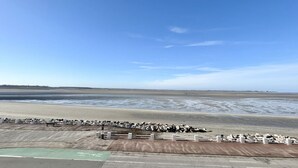 Een kustgebied met een zandstrand, een betonnen pad en een witte hek.