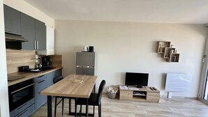 Een moderne keuken met een eettafel, stoelen, een koelkast, een koffiezetapparaat en een televisie.