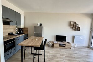 Eine moderne Küche mit Esstisch, Stühlen, einem Kühlschrank, einer Kaffeemaschine und einem Fernseher.