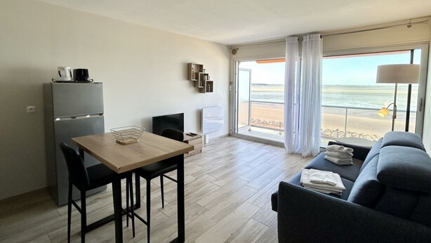 Een kamer met een eettafel, stoelen, een bank, een koelkast en uitzicht op het strand.
