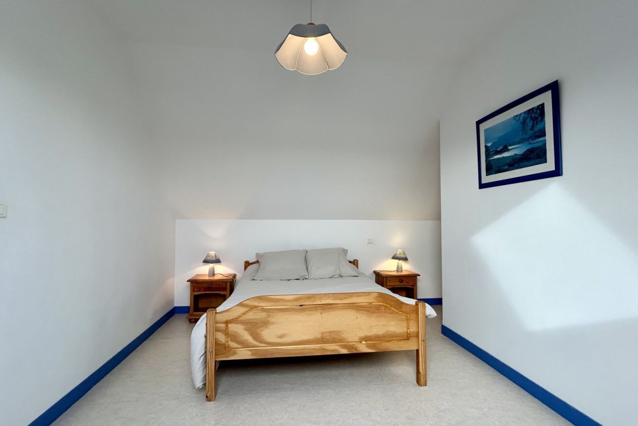 A bedroom with a wooden bed, two bedside tables with lamps, a hanging light fixture, and a framed picture on the wall.