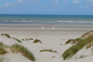 A beach with sand dunes and two white windsurfing boards.