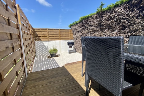 A wooden deck with a wicker chair, a barbecue grill, and a small potted plant.
