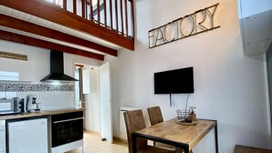 Cocina compacta con zona de comedor, televisor montado en la pared y escalera que sube a un nivel superior.