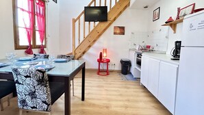 Un coin repas avec une table dressée pour quatre personnes, une cuisine avec des meubles blancs, un escalier en bois et un téléviseur fixé au mur.
