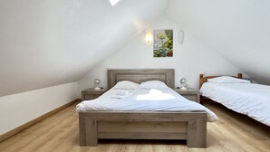 Une chambre à coucher avec un plafond en pente, un lit, des tables de chevet et un luminaire fixé au mur.
