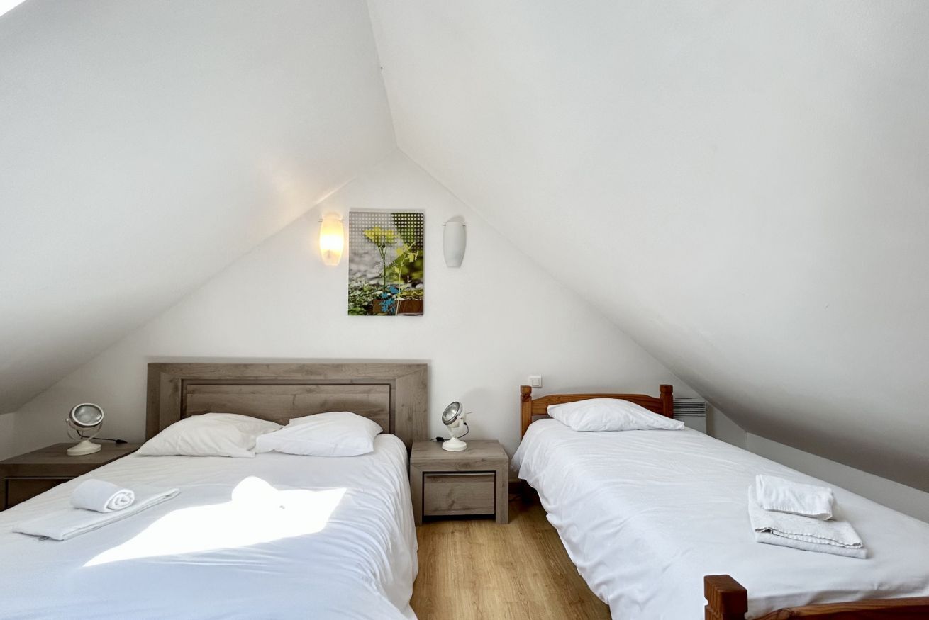 Habitació petita i ben il·luminada amb dues lliteres, una petita taula de nit amb una làmpada, un quadre penjat a la paret i una làmpada al sostre.