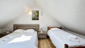 Une petite pièce bien éclairée, avec deux lits, une table de chevet avec une lampe, un tableau accroché au mur et un luminaire au plafond.