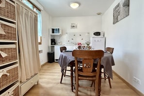 Une cuisine compacte équipée d’un four à micro-ondes, d’une bouilloire et d’une machine à café. On y trouve une table à manger avec des chaises et un meuble de rangement en osier.