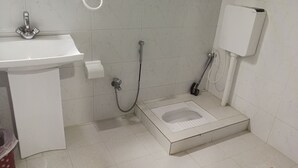 Une salle de bain avec un lavabo, des toilettes, une douche et un seau bleu.