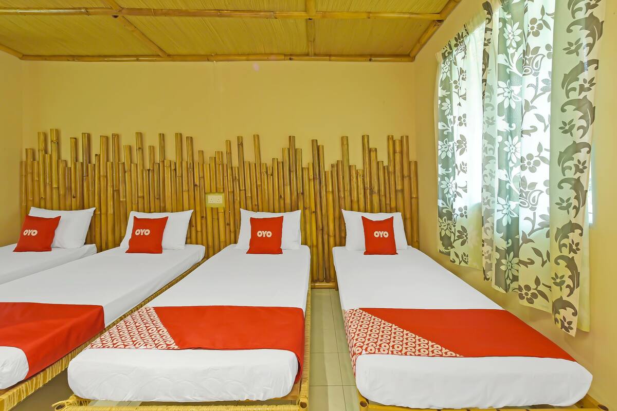 A room with two beds, each with white bedding and red pillows, and a bamboo headboard.
