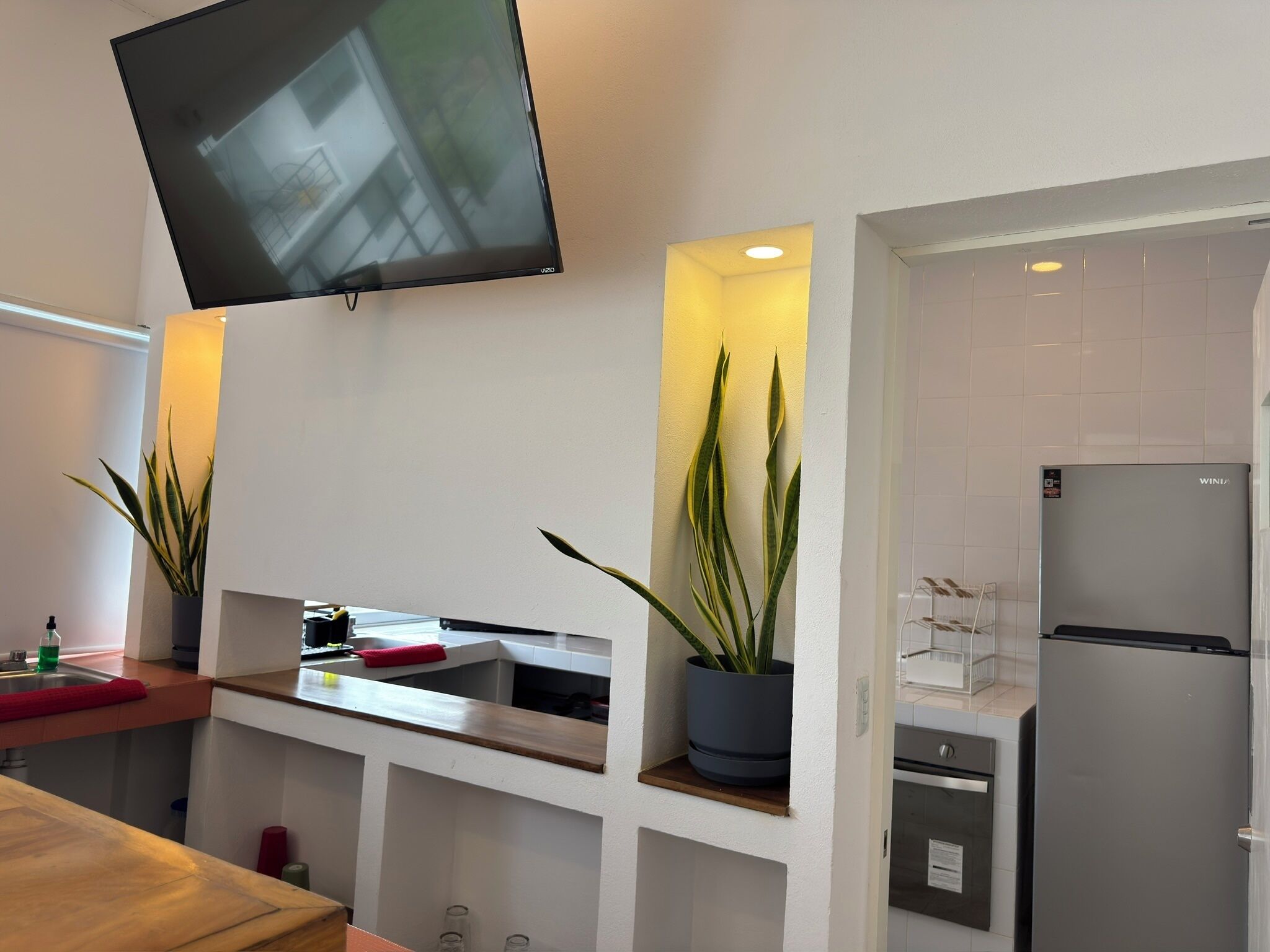 Una cocina moderna con televisor integrado, refrigerador y plantas en macetas.