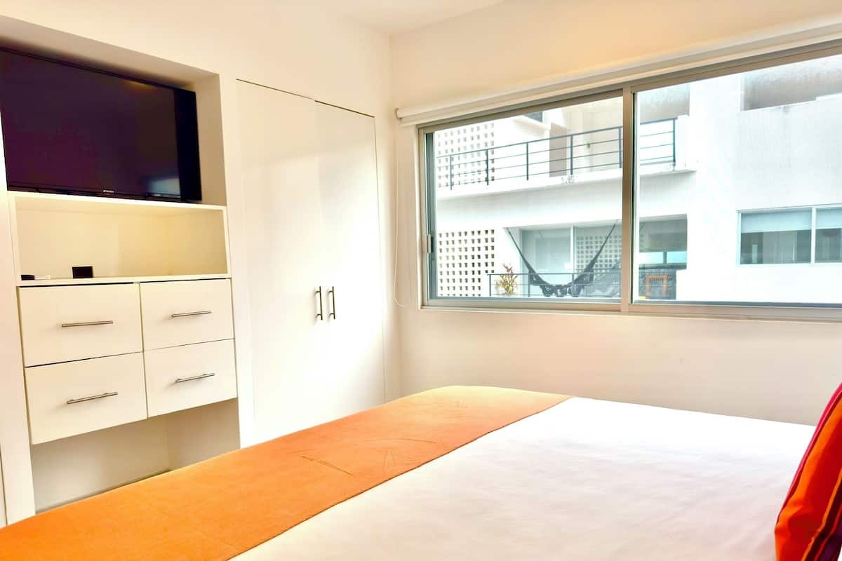 Una habitación de hotel moderna con cama, televisor montado en la pared y ventana con vista al exterior del edificio.