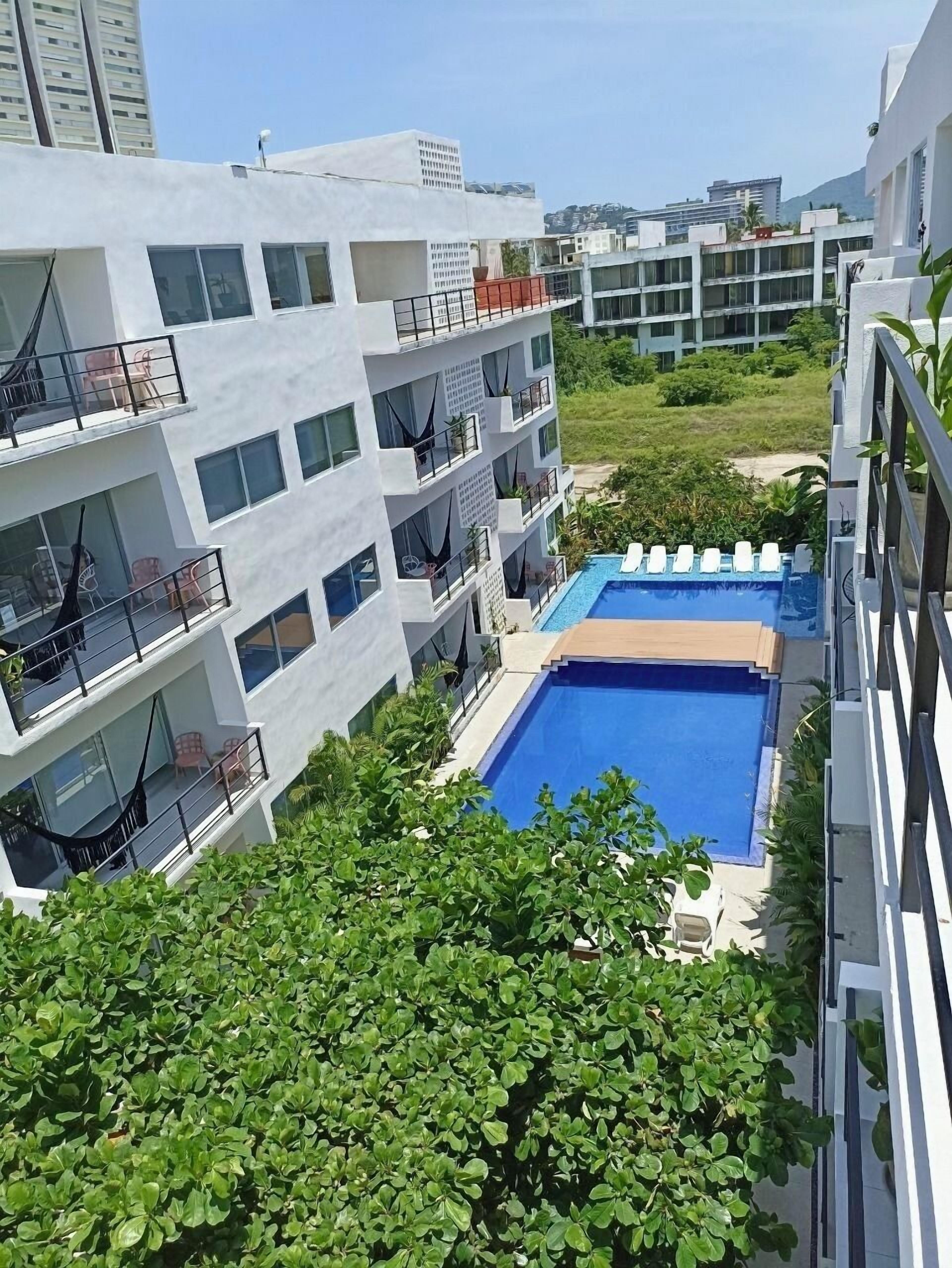 Un edificio moderno con varios balcones, piscina y abundante vegetación.