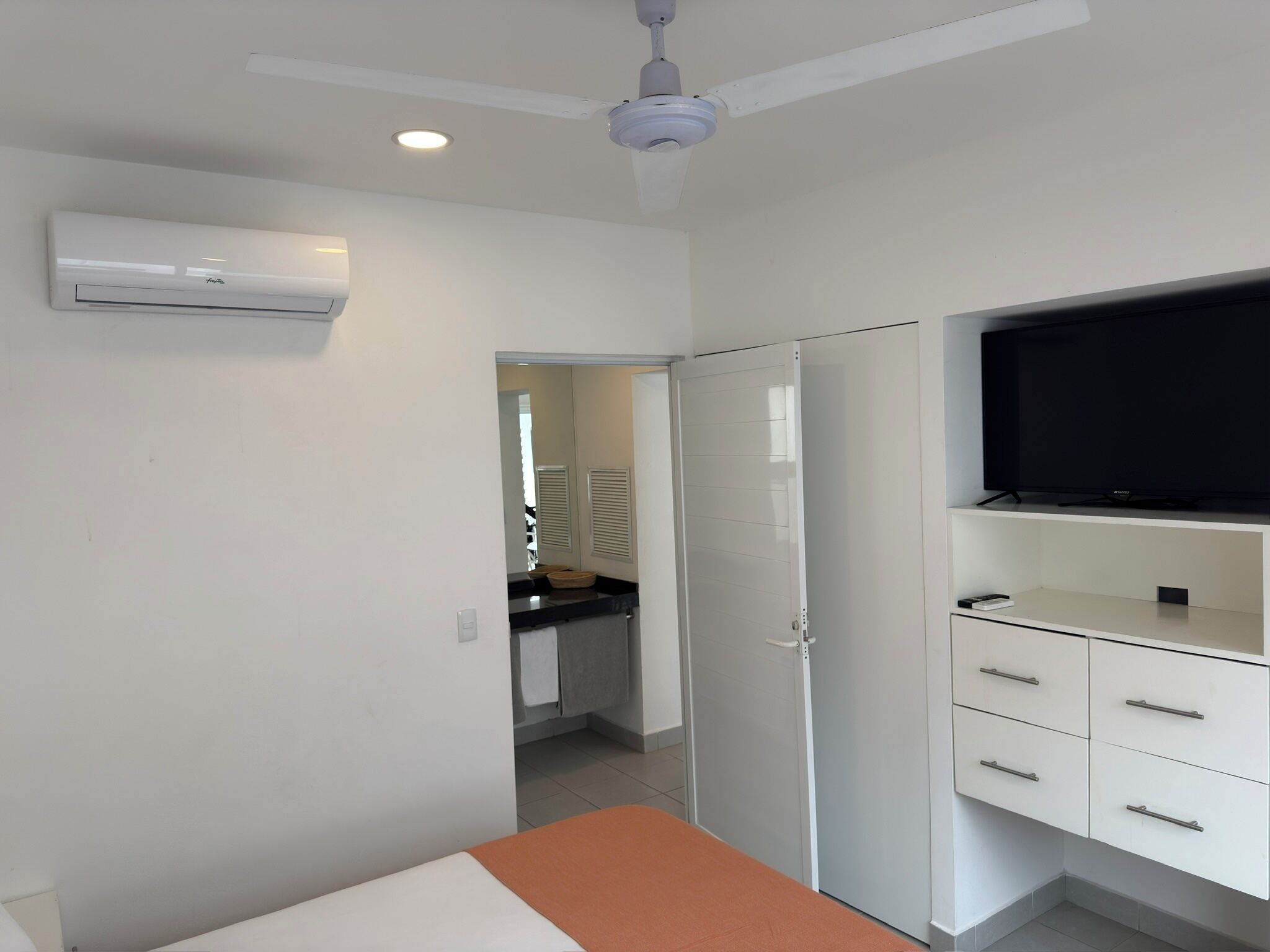 A bedroom with a bed, a TV, a wardrobe, and an air conditioning unit.