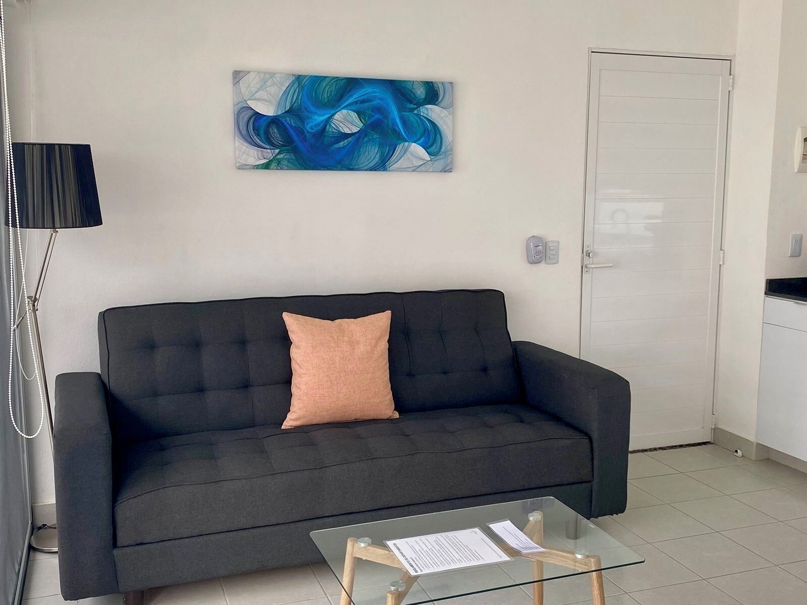 A modern living room with a dark grey sofa, a glass coffee table, and a blue abstract painting on the wall.