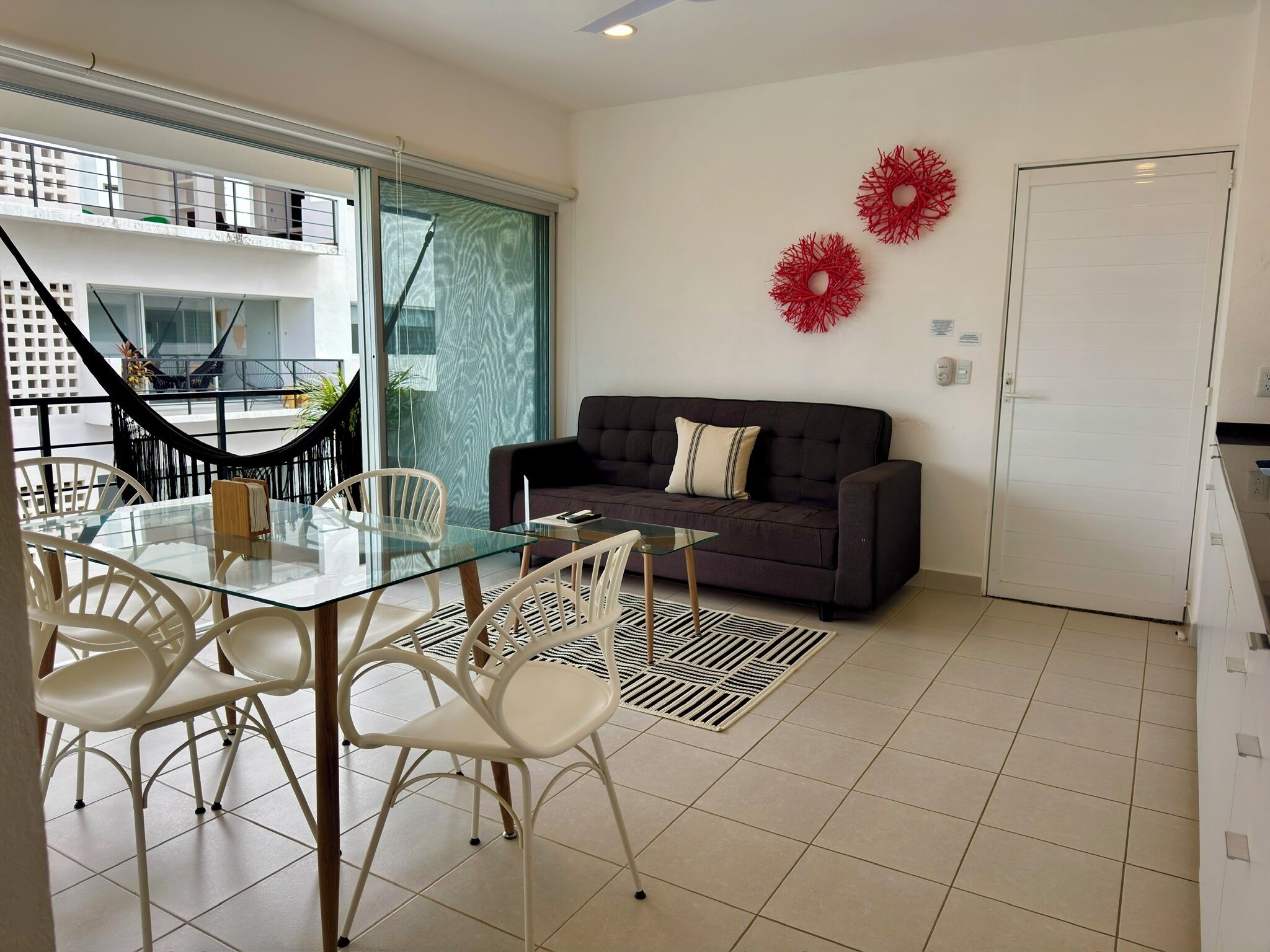 A modern living room with a glass dining table, white chairs, a dark sofa, and a red decorative item on the wall.