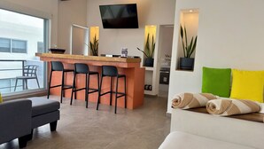 Ein modernes Hotelzimmer mit Bar, einer Couch, einem Esstisch und einem an der Wand befestigten Fernseher.