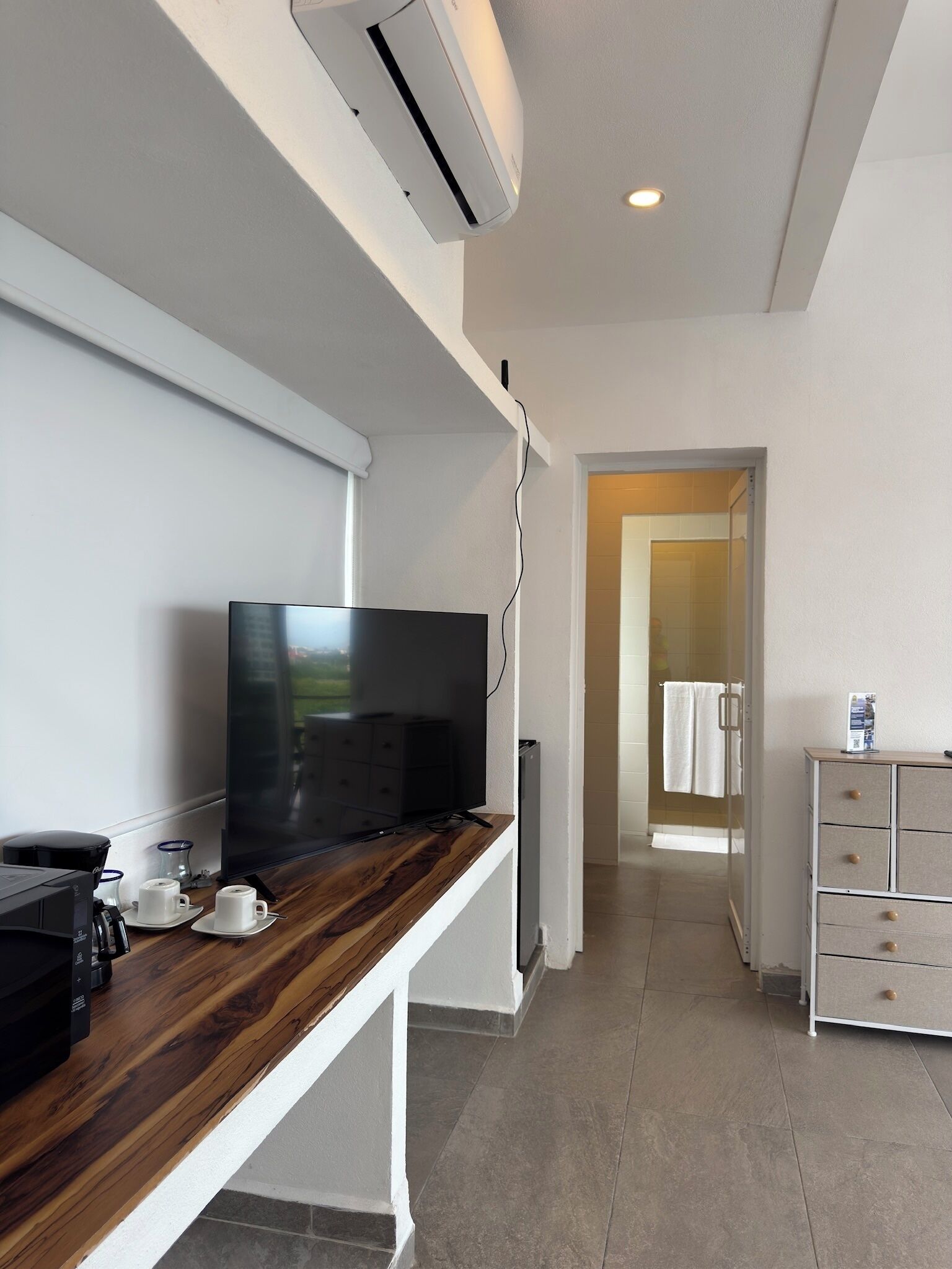 A modern hotel room with a flat-screen TV on a wooden console, a coffee machine, and a white cabinet with drawers.