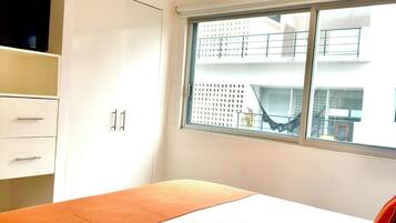 Un dormitorio con cama, ventana con vista a edificios y ventilador de techo.