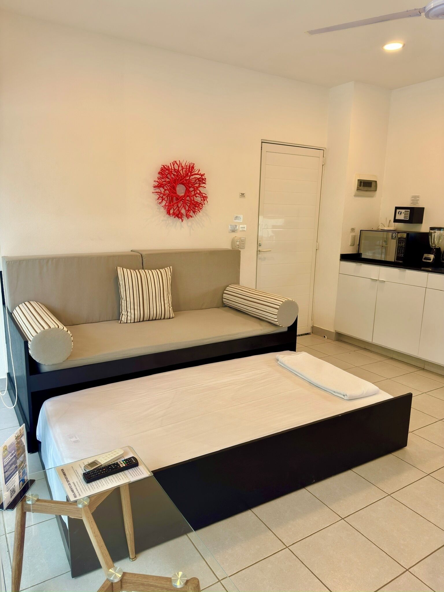 A compact room with a bed, a sofa, a small table, a microwave, and a red decorative item on the wall.