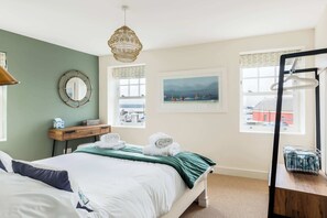A neatly arranged bedroom with a bed, a bedside table, a hanging light fixture, a window with a view, and a wall-mounted mirror.